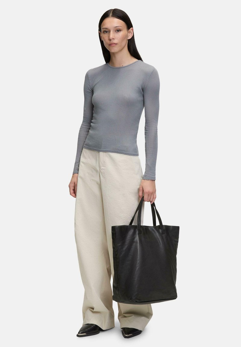 Haut à manches longues gris côtelé associé à un pantalon large crème ; tenant un sac fourre-tout en cuir noir. Textures lisses avec un design structuré.