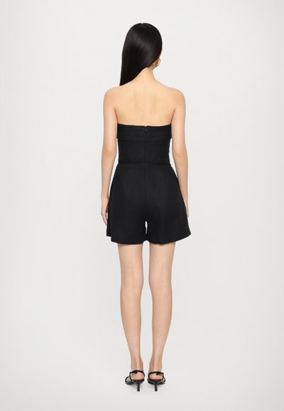 Melnā strapless romper ar pieguļošu bodices un brīviem šortiem. Ar struktūrētu audumu, slēptu aizmugurējo rāvējslēdzēju un gludu apdari. Atvērta aizmugures dizains.