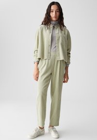 Giacca in velluto a coste verde chiaro e pantaloni abbinati con una vestibilità rilassata, abbinati a un dolcevita grigio. Sneakers bianche completano l'outfit.