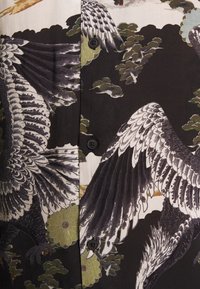 Czarna koszula zapinana na guziki z szczegółowym wzorem ptaków i liści w odcieniach bieli, szarości i zieleni, o gładkiej teksturze i miękkim materiale.