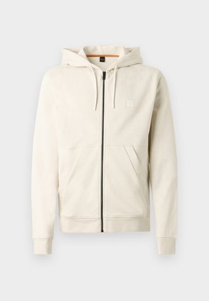 Világos bézs kapucnis pulóver, puha anyagból készült, elöl cipzáros, dupla zsebbel és állítható húzózsinórral a kapucnin. Az mellrészen egyszerű logó található.