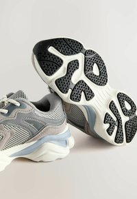 Szare siateczkowe sneakersy z zamszowymi akcentami, z grubą białą podeszwą środkową i czarną teksturowaną podeszwą zewnętrzną. Szczegółowe przeszycia na cholewie.
