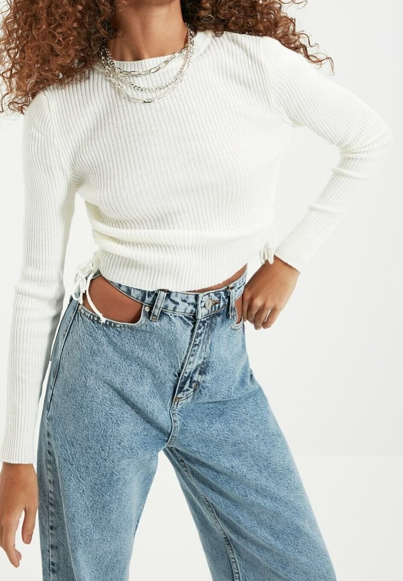 Haut blanc à manches longues côtelé avec des liens sur les côtés et jean denim bleu taille haute. Accents usés et shorts à coupe décontractée.