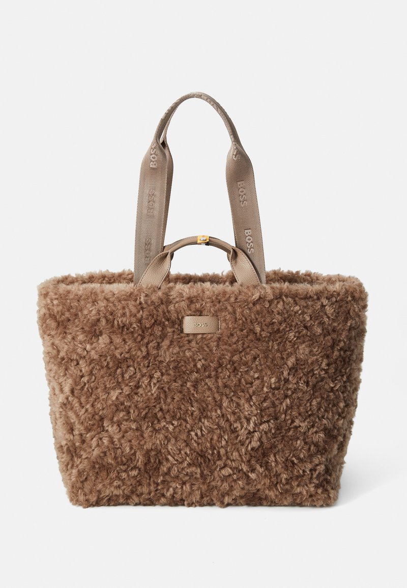 Bruine fluffy draagtas met een zachte textuur, voorzien van lichtbruine handvatten met een gegraveerd logo en een subtiele gouden accenten op de sluiting.