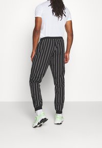 Musta-valkoiset raidalliset juoksuhousut, joissa on joustava vyötärönauha ja lahkeensuut, kevyestä kankaasta ja rento malli.