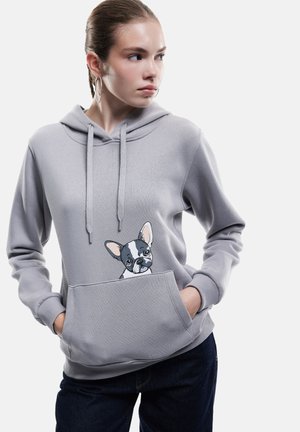 Felpa grigia con cappuccio dotata di tasca frontale e illustrazione di un cane sul petto. Il materiale sembra morbido, con una vestibilità comoda e cappuccio regolabile.