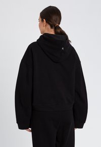 Felpa nera corta con cappuccio, vestibilità oversize, materiale in morbido cotone, dotata di cappuccio con coulisse e piccolo dettaglio logo sul retro.