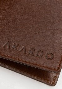 Hnedá kožená peňaženka s textúrovaným povrchom, s embosovaným logom 'AKARDO' a viditeľným šitím pozdĺž okrajov.