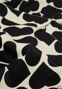 Zwart-wit stof met grote hartvormige patronen, gladde textuur, met goudkleurige knoppen in de vorm van hartjes als accenten.