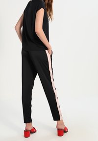 Sort kortærmet top parret med sorte bukser med en pink sidelæbe; modellen bærer røde blokhæle sandals. Glat stof, afslappet pasform.