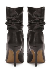 Melna ādas slouchy pusgarā zābaku pāris ar uzgāztām augstajām stiletto papēžiem, skatoties no aizmugures.