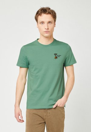T-shirt verde in cotone con maniche corte, scollatura tonda e un piccolo grafico ricamato che presenta il testo “Vegetally Yours” e un design di foglia.