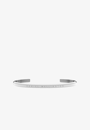 Stříbrný náramek s hladkým, minimalistickým designem. Obsahuje vyryté texty "DANIEL WELLINGTON", hladký metalický povrch a otevřené konce.