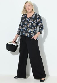 Haut noir à fleurs avec décolleté en V et manches trois-quarts, associé à un pantalon noir à jambes larges. Les accessoires comprennent un sac à main noir et un bracelet.