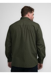 Camisa de manga larga verde con un patrón, cuello, puños abotonados y un corte relajado, que muestra un sutil diseño geométrico en una tela texturizada.