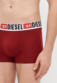 Červené bavlnené boxerky majú hrubý elastický biely pás s čiernym logom. Hladká štruktúra s priliehavým strihom.