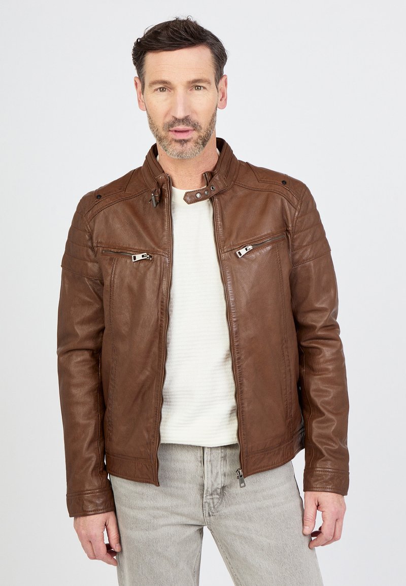 Braune Lederjacke mit hohem Kragen, Reißverschluss und Druckknopfverschlüssen sowie zwei Reißverschlusstaschen auf der Vorderseite. Glatte Textur mit gefältelten Schulterakzenten.