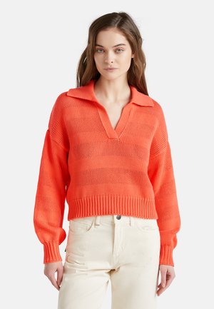 Gebreide v-hals pullover in fel oranje met een kraag, lange mouwen en geribde manchetten en zoom; gecombineerd met off-white broeken.