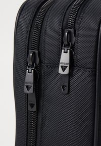 Valigia nera in nylon con doppi zip, caratterizzata da accessori neri con marchio e una finitura texture. Design compatto adatto per i viaggi.