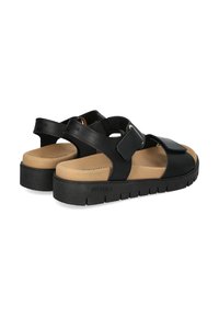 Zwarte leren sandalen met verstelbare banden, tan voetbed, getextureerde zwarte rubberen zool en subtiele branding op de hiel.
