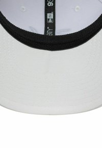 Weißes Baseballcap mit einem schwarzen Schild, ausgestattet mit einer strukturierten Innenseite und Belüftungsöffnungen, innen mit einem Markenlabel versehen.
