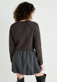 Suéter castanho tricotado com mangas raglan, combinado com uma saia evasê de riscas pretas e brancas. Textura suave com um silhueta descontraída.