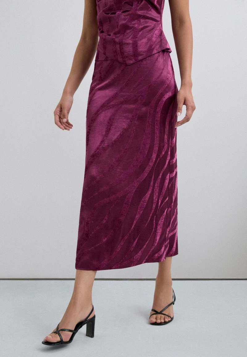 Falda de satén color ciruela hasta la rodilla con textura ondulada y ligero brillo; combinada con tacones negros con tiras. Diseño simple y ajustado que realza la silueta.