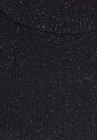 Tissu noir côtelé avec des fils argentés étincelants tissés partout, montrant la texture et la brillance.