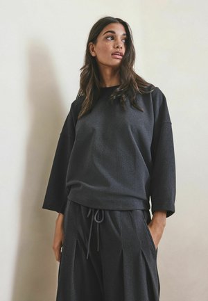 Dark gray wide-sleeve sweatshirt made from textured fabric, paired with matching drawstring pants featuring pleats and side pockets.