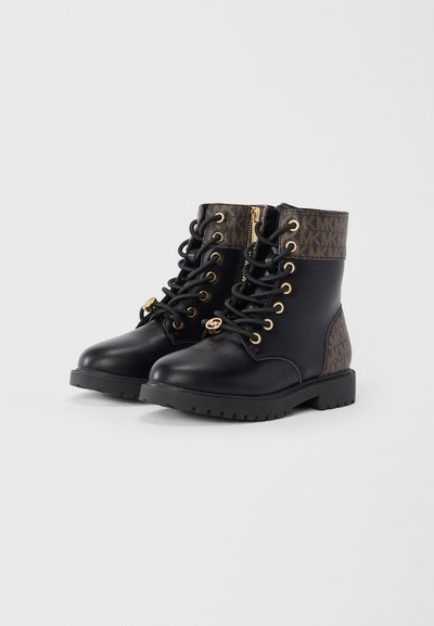 Bottes noires à la cheville avec lacets, quincaillerie dorée et tige en cuir texturé marron présentant un motif de logo. Semelles en caoutchouc avec un profil robuste.