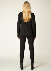 Zwarte top met lange mouwen in combinatie met zwarte strakke broek. De stof lijkt soepel en rekbaar, met een eenvoudig, tailormade ontwerp en minimale accenten.