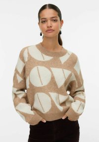 Pull en beige et crème avec des motifs géométriques, fabriqué en tissu doux, doté d'un col rond et de poignets côtelés, associé à un pantalon noir.