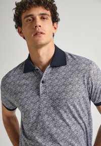 Polo tričko s navy a bílým vzorem, s límečkem, krátkými rukávy a dvouknoflíkovou légou, vyrobené z prodyšného materiálu.