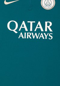 Teal urheilu pelipaita, jossa on puolivetoketju, valkoisella "QATAR AIRWAYS" -logolla ja pyöreällä PSG-logolla. Pehmeä kangas, minimalistinen muotoilu.