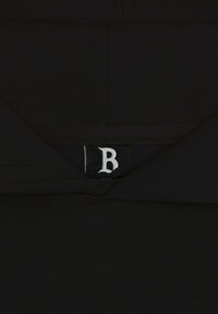 Schwarzes Kleidungsstück mit strukturiertem Finish, das ein sichtbares Etikett mit dem Buchstaben "B" zeigt. Das Design ist minimalistisch und hat nahtlose Kanten.