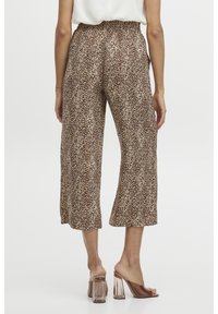 Spodnie 3/4 w luźnym kroju w panterkę w odcieniach brązu i beżu, z elastycznym pasem i gładkiego materiału, zestawione z przezroczystymi sandałami na obcasie.