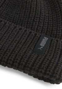 Strikket sort beanie-hat med ribbet tekstur. Den har et lille sort mærke med hvidt brandlogo. Materialet virker varmt og tykt.
