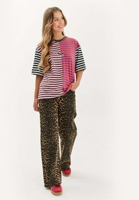 Pasiasty t-shirt z krótkim rękawem w kolorze różowym, fioletowym i czarnym z grafiką motyla. W zestawie z szerokimi spodniami w panterkę i czerwonymi butami.