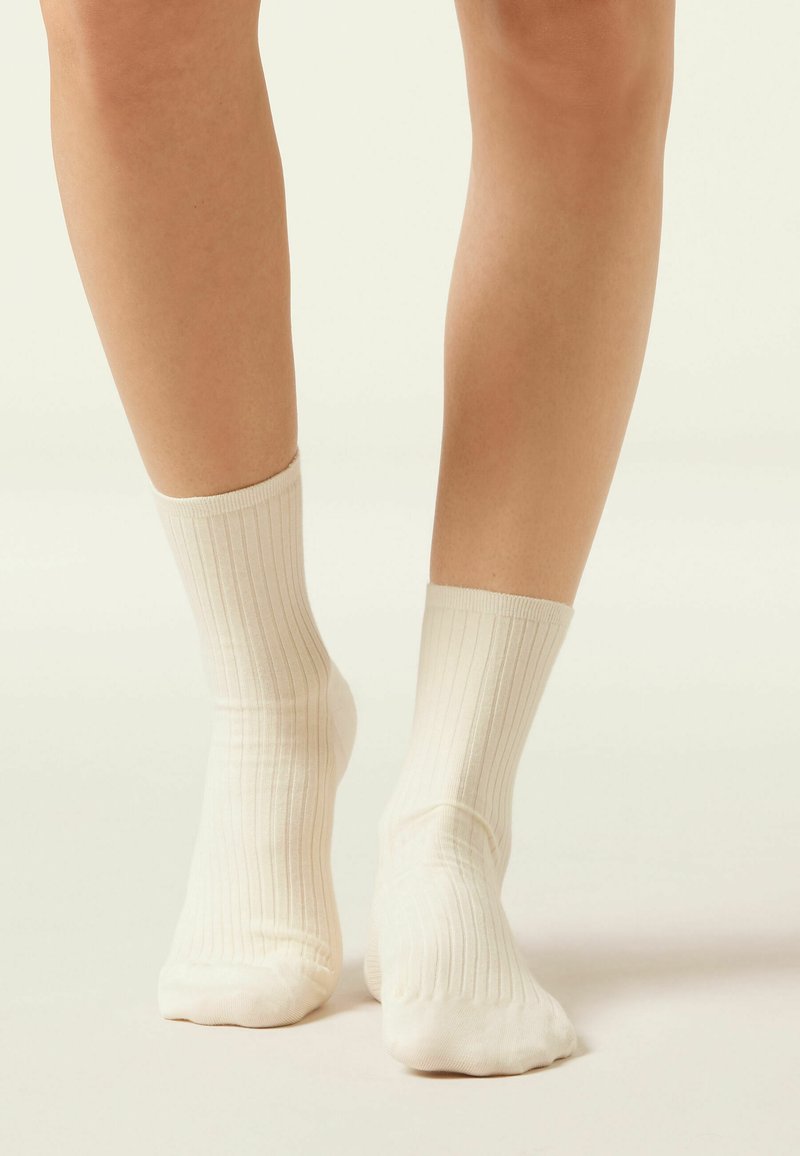 Chaussettes côtelées jusqu'aux genoux de couleur crème clair, fabriquées en tissu doux, avec un bracelet extensible et une texture lisse. Design uni sans motifs.