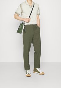 Khaki kalhoty, světle béžové polo, zelená crossbody taška a zelené vysoce střižené tenisky s bílými a béžovými akcenty. Hladký a přiléhavý střih.