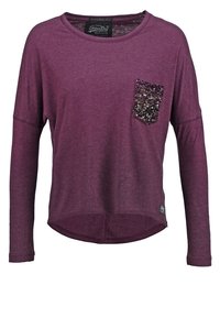 Lila Langarmshirt mit rundem Halsausschnitt und einem mit Pailletten verzierten Taschen-Detail. Weicher Stoff mit einem leicht abgerundeten Saum.