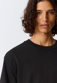 Čierne bavlnené tričko s výstrihom do kruhu, krátkymi rukávmi a voľným strihom; hladká textura a rovnomerný povrch bez vzorov alebo akcentov.