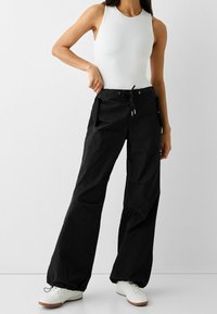 Svarta, vida byxor i lätt tyg, med elastisk midja och dragsko samt sidofickor. Vita sportskor.