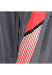Manga de chaqueta gris oscuro con un bolsillo vertical y un diseño de rayas rojas, negras y reflectantes en el brazo.