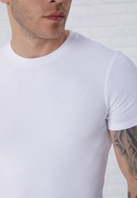 Weißes, geripptes, kurzärmeliges T-Shirt mit Rundhalsausschnitt. Es zeichnet sich durch eine figurbetonte Passform und eine glatte Textur aus, die die Dehnbarkeit des Materials hervorhebt.