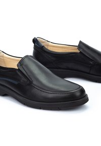 Zapatos negros sin cordones hechos de cuero suave, con punta redondeada, detalles de costura sutiles y un interior acolchado para mayor comodidad.
