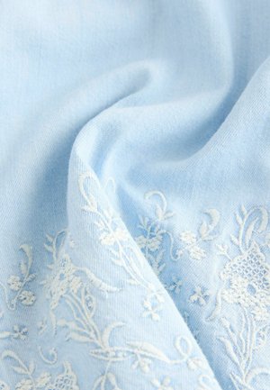 Light blue fabric with soft texture, featuring white floral embroidery with intricate patterns. The fabric drapes gently, creating soft folds.