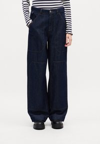 Bredde ben mørkeblå denimbukser med store lommer og kontraststing, med høy midje og avslappet passform.