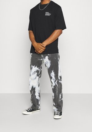 Camiseta de algodón negra de manga corta con texto blanco. Jeans grises con un patrón nublado en blanco y negro. Zapatillas negras con suela blanca.