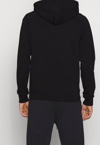 Svart hoodie med dragsko i huvan, raglanärmar samt ribbad mudd i ärmslut och fåll. Tillverkad av ett mjukt och slätt tyg. Inga synliga logotyper eller mönster.